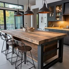 a kitchen island with stools and lights hanging from it's sides in front of an open floor plan