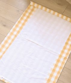 an orange and white checkered tablecloth laying on the floor next to a cat