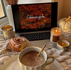 a cup of hot chocolate next to a laptop on a table with candles and cinnamon rolls