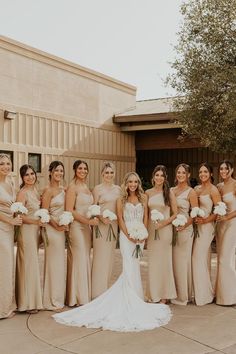 a group of women standing next to each other in front of a building holding bouquets