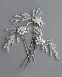 three silver hair pins with pearls and leaves on them, set against a gray background