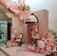 a pink room with balloons and chandeliers on the ceiling, in front of a staircase