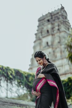 a woman in a black sari standing next to a tall building with a clock tower behind her