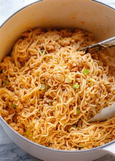 a pot filled with noodles and vegetables on top of a marble countertop next to a wooden spoon