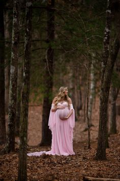 a pregnant woman in a pink gown standing in the woods with her hands on her belly