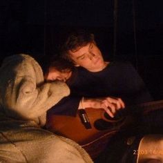 a man and woman sitting next to each other with a guitar in front of them