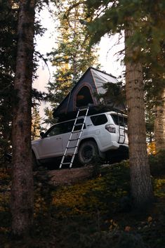 a white truck parked in the woods with a tent on top