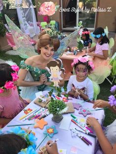 a group of children sitting around a table with fairy decorations on it's head