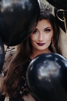 a woman with long hair and purple lipstick is surrounded by black balloons