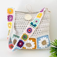 a crocheted purse with a button on the front and strap around it, sitting next to a potted plant