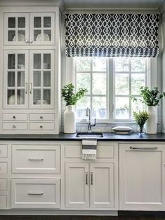 a kitchen with white cabinets and black counter tops next to a window covered in curtains