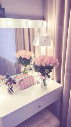 a white vanity with flowers on it in front of a mirror and lights above it