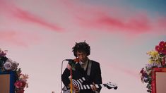 a man with dreadlocks on his head playing an electric guitar in front of flowers