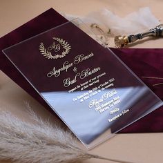 an elegant wedding card with gold lettering and a purple cover is on the table next to some feathers