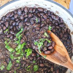 a wooden spoon in a pot filled with black beans and cilantro leaves on the side