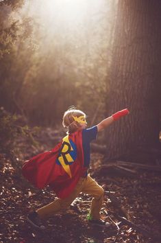 a young boy dressed as superman running through the woods