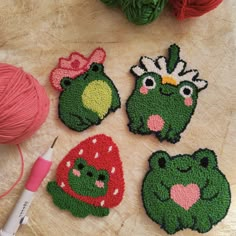 four crocheted frog coasters sitting on top of a table next to a ball of yarn