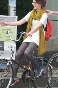 a woman in tights riding a bike on the street with her hand out to someone