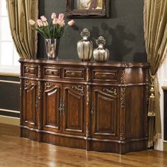 a wooden sideboard with vases and flowers on it in front of a painting