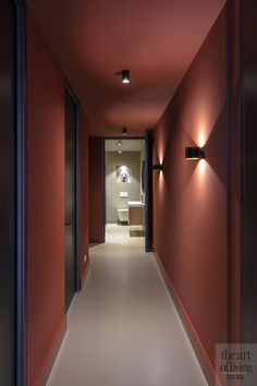 a long hallway with red walls and lights on the side wall, leading to a bathroom