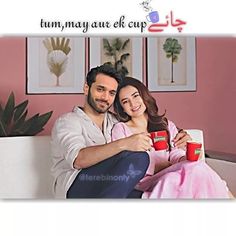 a man and woman sitting on a couch holding coffee mugs in front of their faces