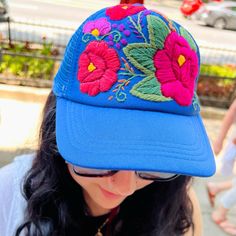 a woman wearing a blue hat with flowers on the front and side, while looking down at her cell phone