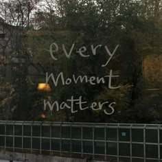 graffiti written on the side of a building that says every moment matters, with trees in the background