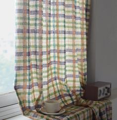 a cup and saucer sitting on top of a window sill next to a curtain