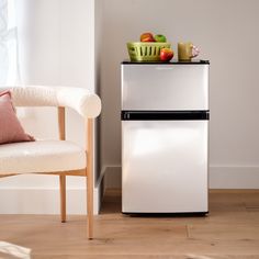 a small white refrigerator sitting next to a chair