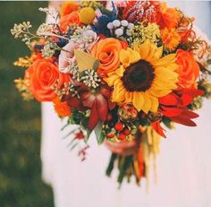 a bridal bouquet with sunflowers, roses and other flowers is held by a woman