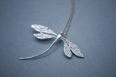 a silver necklace with two leaves hanging from it's center, on a gray surface