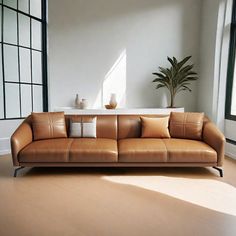 a brown leather couch sitting on top of a hard wood floor next to a window