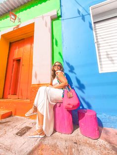 a woman sitting on top of two pink stools in front of a colorful building