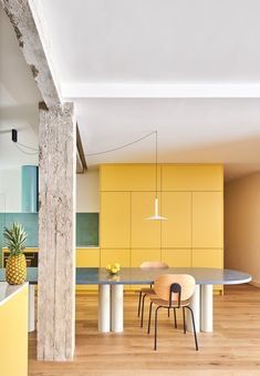 a dining room table with chairs and a pineapple in the center is surrounded by yellow cabinets