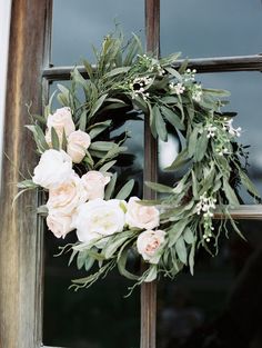 a wreath with white flowers and greenery hanging on a window sill