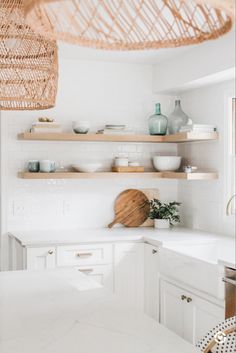 a white kitchen with open shelves and wicker baskets hanging from the ceiling over the counter