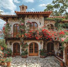 a stone house with red flowers on the balconies and potted plants in front