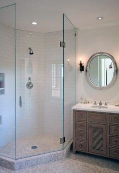 a bathroom with a walk in shower next to a double sink vanity under a round mirror