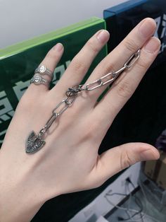 a person's hand with two rings and chains on it, in front of a green box