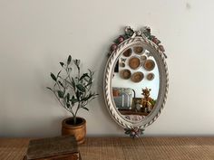 a mirror sitting on top of a wooden table next to a potted plant and vase