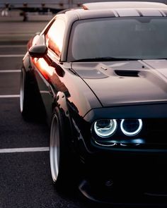 the front end of a black car in a parking lot with its lights turned on