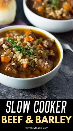 two bowls of slow cooker beef and barley soup on a table with bread in the background