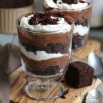 two glasses filled with dessert sitting on top of a wooden cutting board