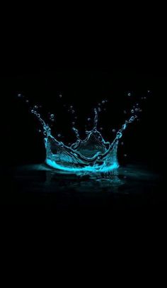 a blue water splashing on top of a black surface in the dark with no one around it