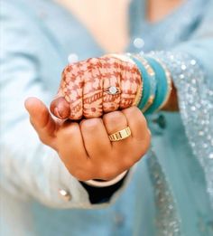 a close up of a person's hand holding a ring and wearing a blue dress