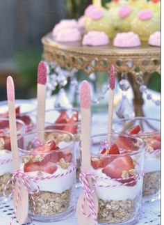 strawberries are in small cups with spoons on a doily covered tablecloth