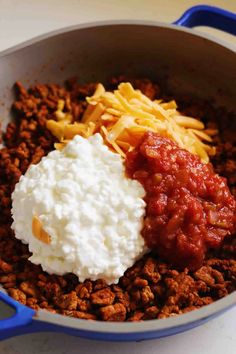 some food is in a blue pan on the table and it looks like chili, cheese, and sour cream