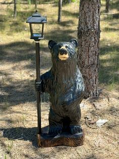 a statue of a bear holding a lamppost in the woods next to a tree