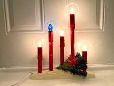 three red candles are sitting on a table next to a wreath and some lights in the shape of christmas balls