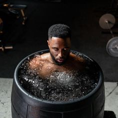 a man sitting in a large black barrel filled with water and looking at the camera